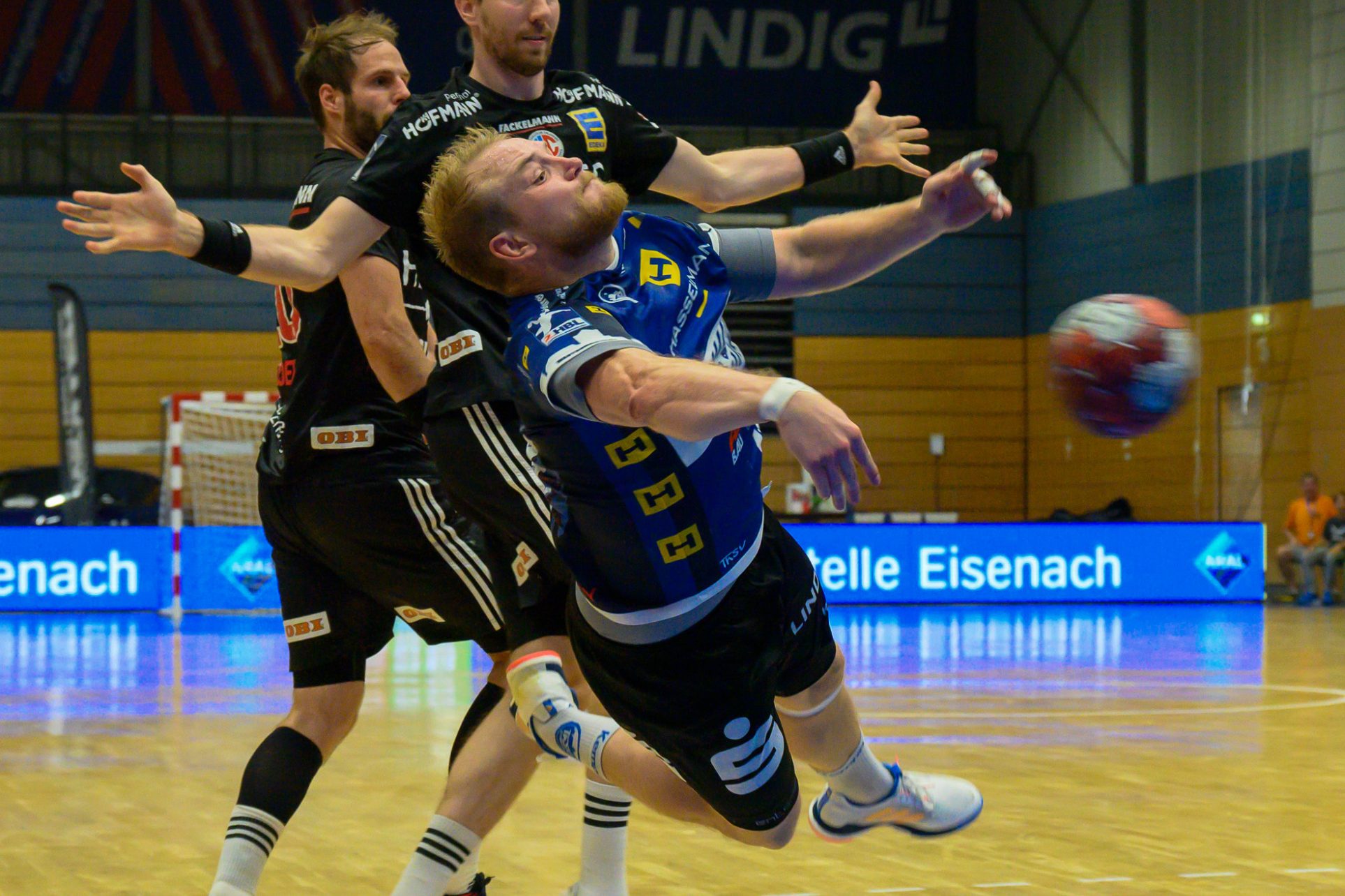 Handball Handballspieler springt zum Wurf, während zwei Verteidiger ihn angreifen.