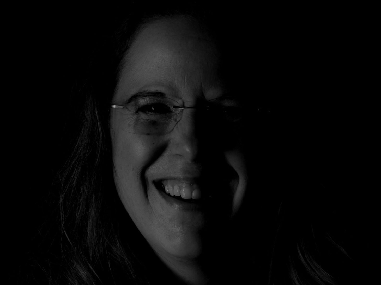 Fotostudio Lächelnde Person mit Brille vor dunklem Hintergrund.